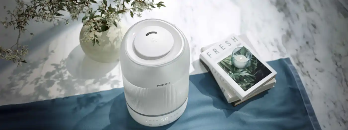 Air-Humidifier-1-fi Produkta fotoattēls: balts Philips gaisa mitrinātājs uz zilas virsmas. Šis augstākās klases Climate Care risinājums demonstrē uz lietotāju orientētu tehnoloģiju, kas nodrošina optimālu mitruma līmeni un izcilu iekštelpu pieredzi.