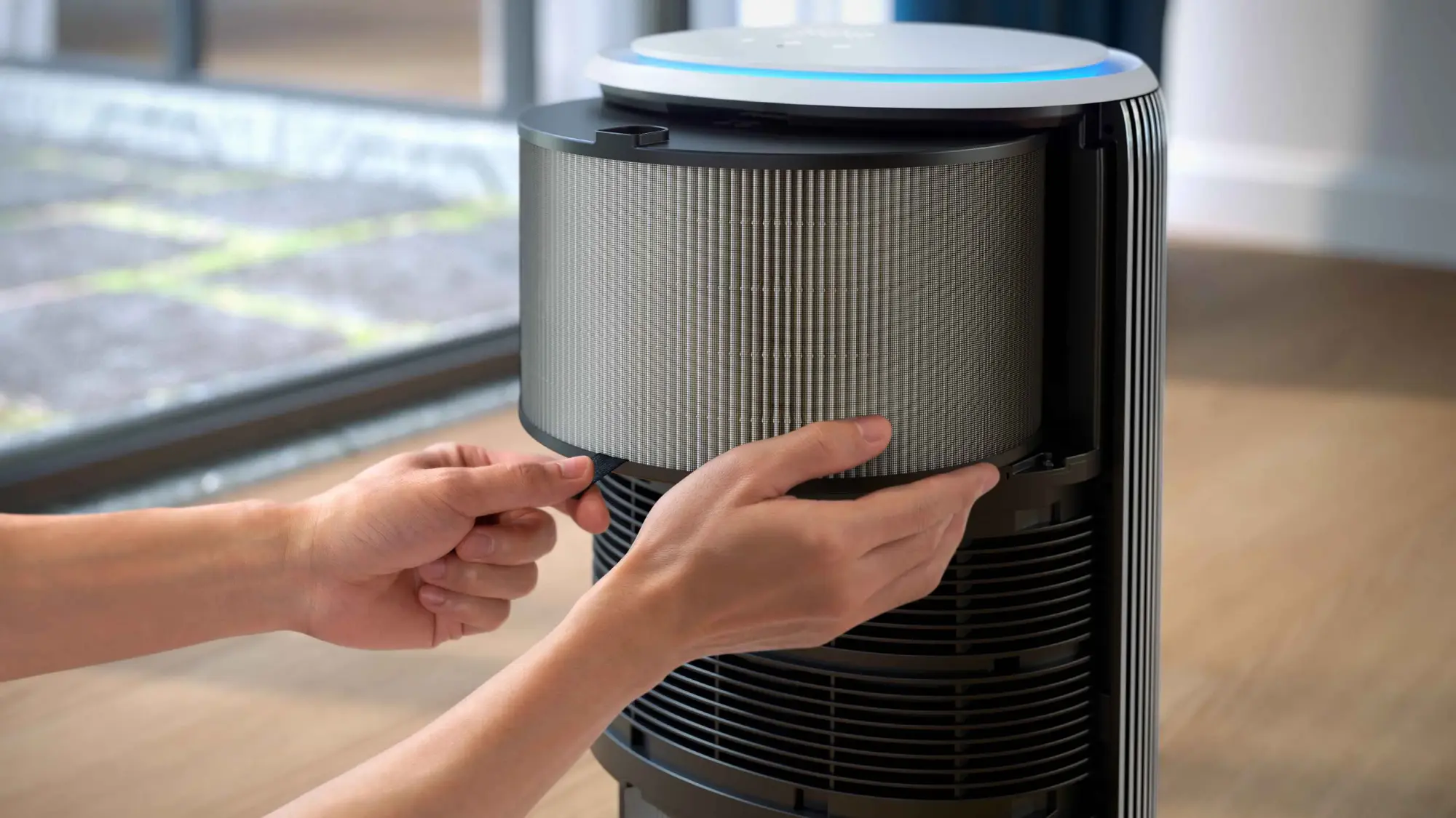 Air-Purification-14-fi Rokas, kas rāda filtra nomaiņu Philips gaisa attīrīšanas sistēmā. Climate Care dizains ar zilu akcentu, cilindrisks filtrs izcilai gaisa kvalitātei. Uzlabota dzīve.