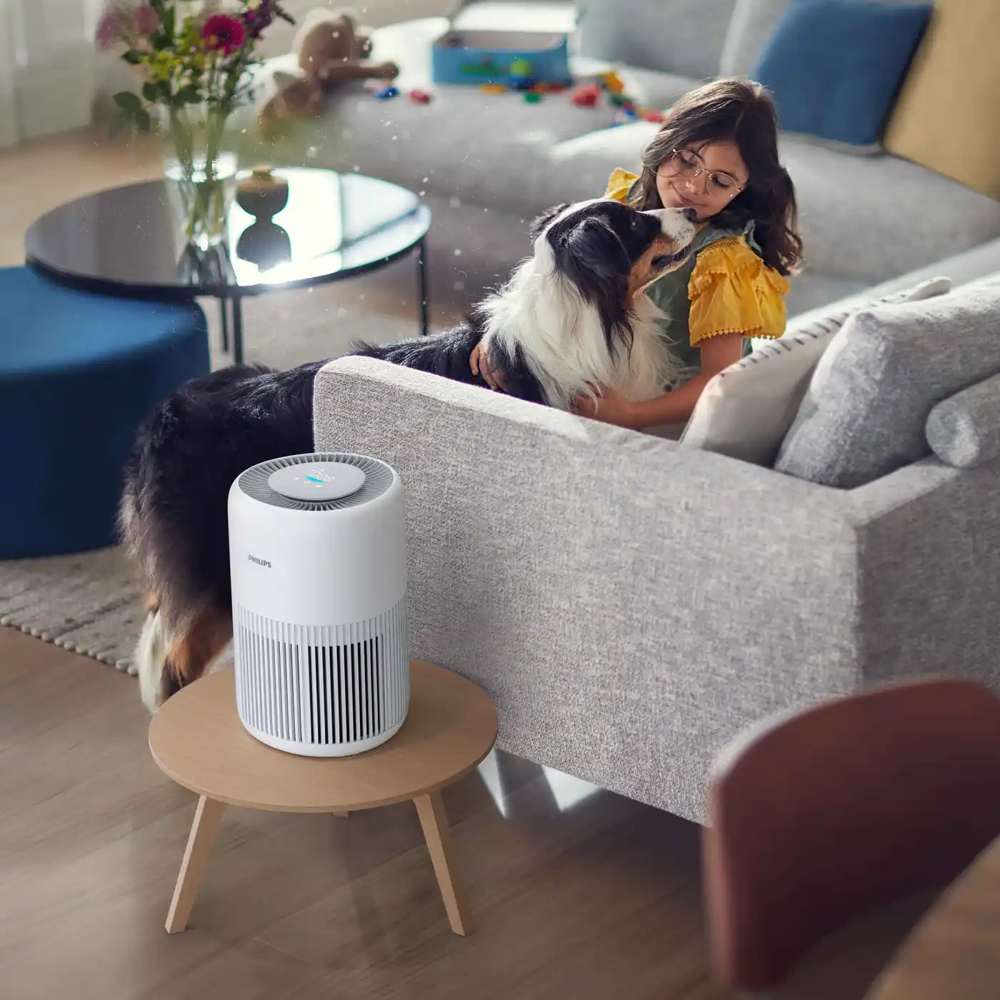 Air-Purification-2-fi Philips gaisa attīrīšanas iekārtas veicina izcilu gaisa kvalitāti, ko ilustrē dzīvesveids ar baltu attīrītāju uz galda, meiteni, kas glāsta savu suni; tas viss ilustrē tīru iekštelpu gaisu.