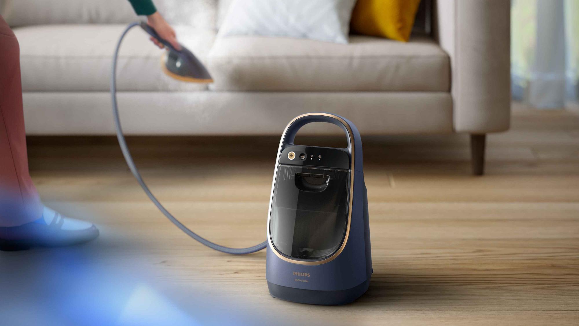 Philips universālais All-in-One apģērbu tvaicētājs ar statīvu tiek izmantots uz dīvāna, demonstrējot tā daudzpusību. Izbaudiet augstākās kvalitātes aprūpi ar Philips universālo tvaikoni visam savam apģērbam un mēbelēm.