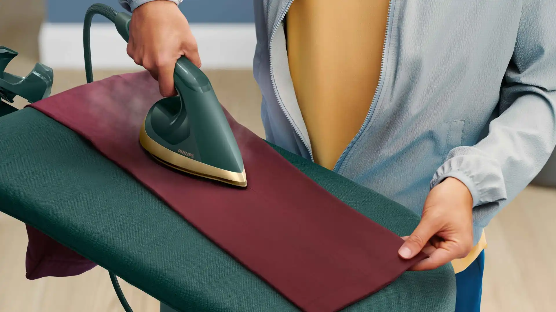Attēlā redzams Philips All-in-One universālais apģērbu kopšanas risinājums — rokas tvaikonis ar tvaika funkciju bordo krāsas audumiem. Kvalitāte un inovatīvs dizains uz moderna gludināmā dēļa.