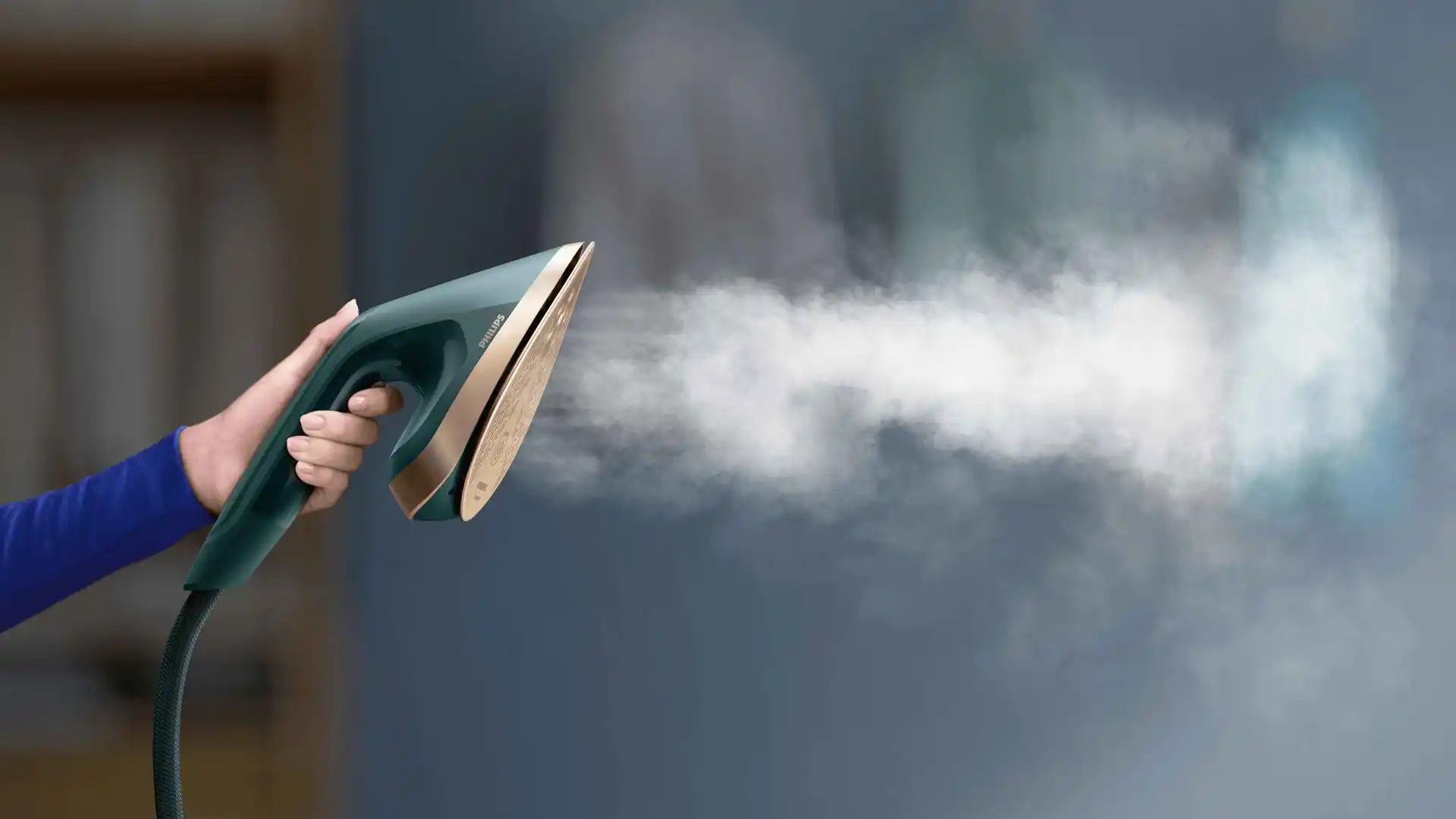 Zilganzaļš Philips All-in-One universālais apģērbu kopšanas tvaikonis, kas izdala tvaiku, turams rokā. Izceļ ierīces moderno dizainu un izcilo tvaika padevi vienkāršai un efektīvai apģērbu kopšanai.