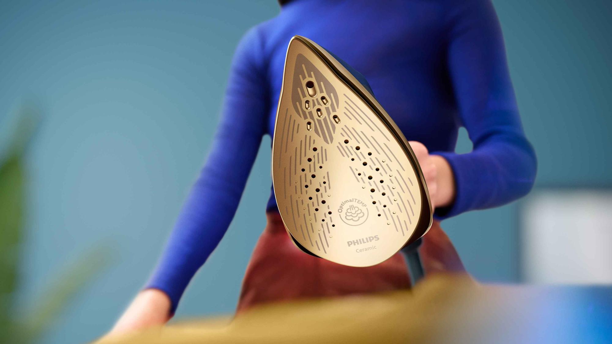 Philips universālā All-in-One apģērbu kopšanas gludekļa tuvplāns, kurā redzama tā augstākās kvalitātes zelta keramikas gludināšanas virsma un optimālās temperatūras tehnoloģija.