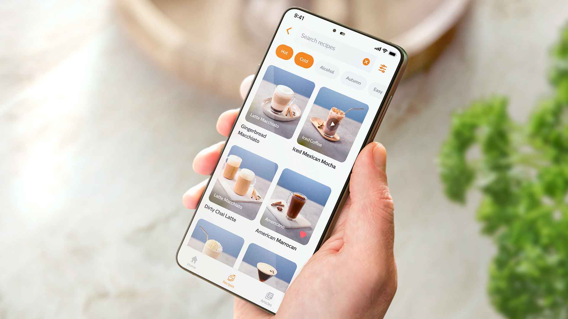 Persona tur viedtālruni, kurā redzama lietotne HomeID ar kafijas dzērienu iespējām.