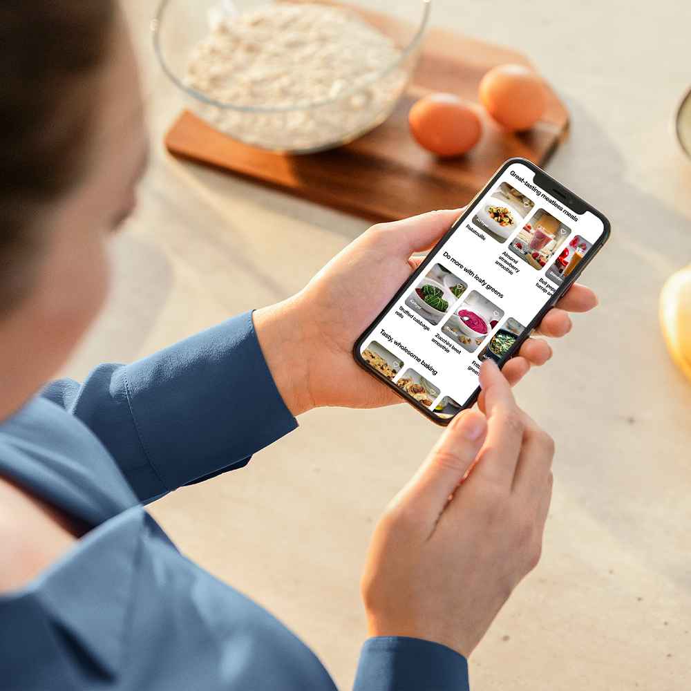 Tuvplāns ar roku, kurā turēts viedtālrunis, kurā redzama gardas mango smūtija bļodas recepte no Philips Blend & Juice lietotnes, demonstrējot tās lietotājam draudzīgo saskarni un iedvesmojošo saturu.