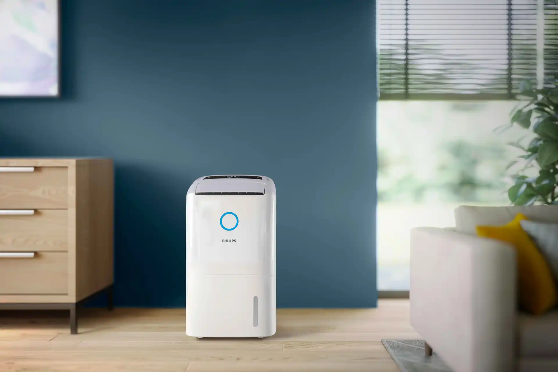 Philips Climate Care gaisa sausinātājs modernā viesistabā ar zilu akcenta sienu. Ievērojiet tā integrēto ūdens līmeņa indikatoru un lietotājam draudzīgo vadību.