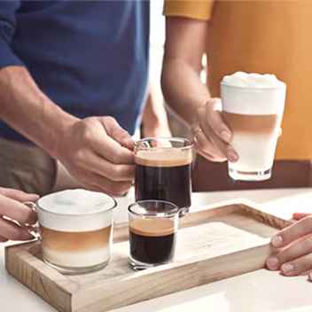 Coffee-22-fi Rokās tur Philips kafijas dzērienus: slāņveida latte macchiato, bagātīgu espresso. Paplātē ir dažādi kafijas veidi, kas uzsver kafijas automāta daudzpusību. Izbaudiet kafijas garšu.