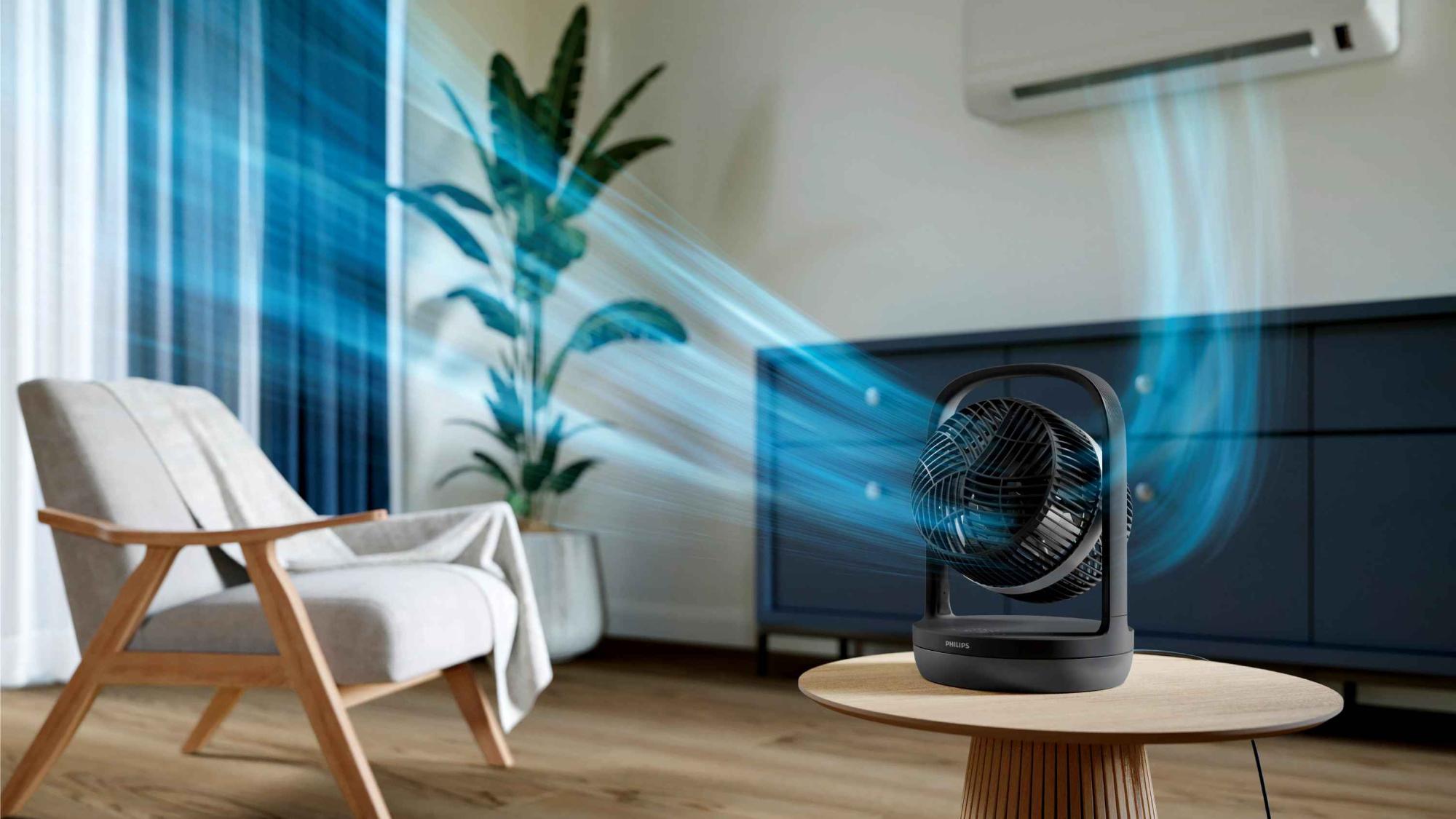 Philips Climate Care dzesēšanas baltais torņa ventilators cirkulē vēsu gaisu gaišā, modernā telpā ar atvērtām balkona durvīm un plūstošiem baltiem aizkariem.