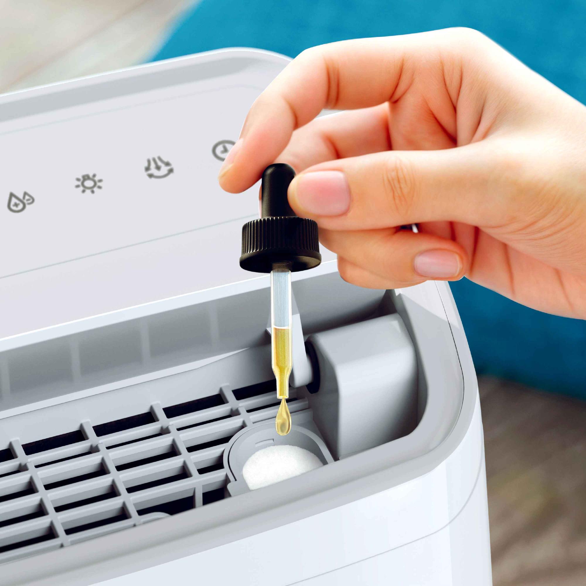 Tuvplāns ar roku, kas pievieno aromātisko eļļu baltajam Philips gaisa sausinātājam. Eļļa krīt uz aromterapijas paliktņa, radot svaigu aromātu, vienlaikus noņemot mitrumu un piedāvājot izcilu lietotāja pieredzi.