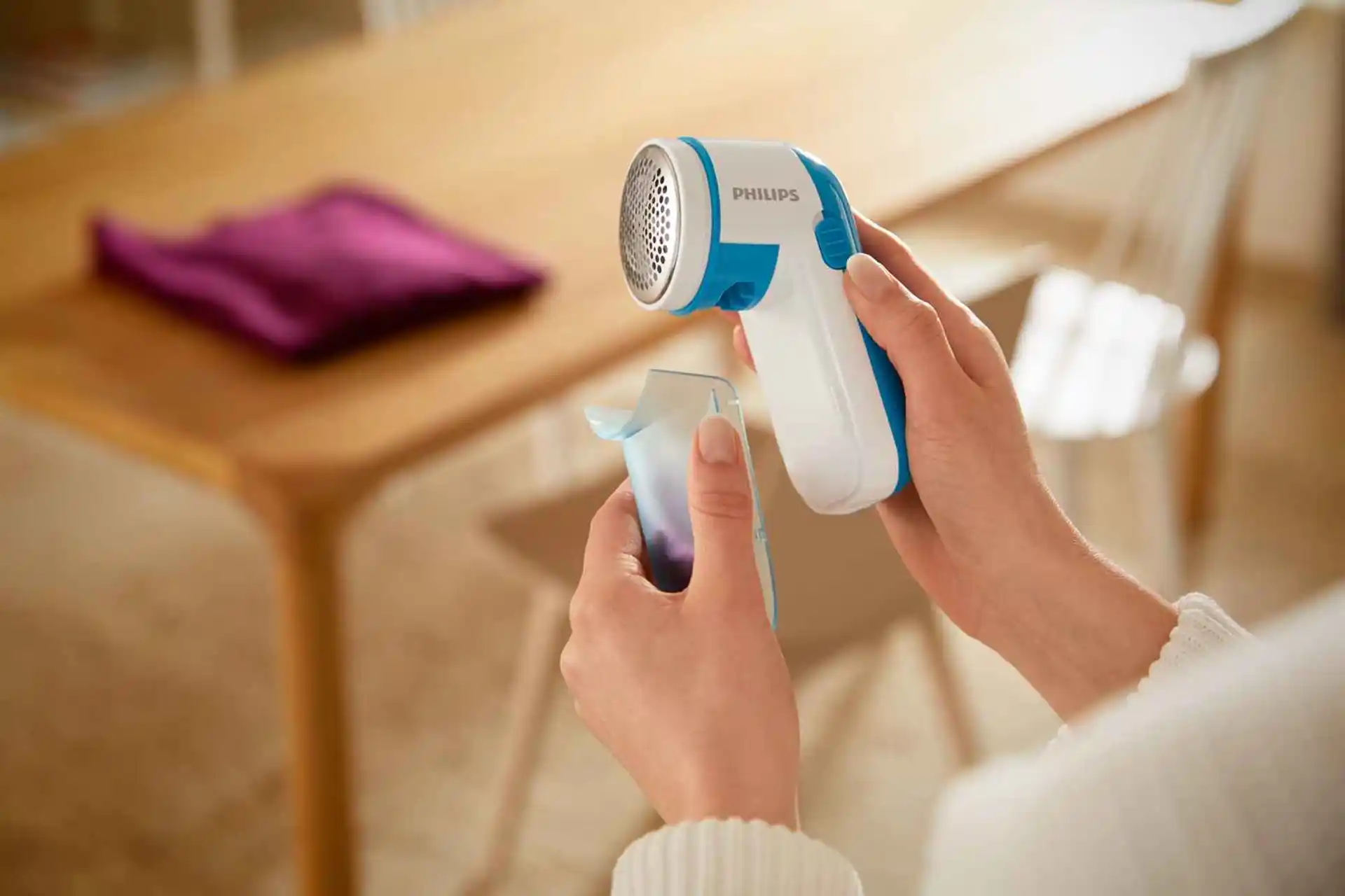 Rokas tur Philips Essentials apģērbu kopšanas līdzekļu skuvekli un pūku savācēju. Baltzilajam skuveklim ir metāla galviņa.