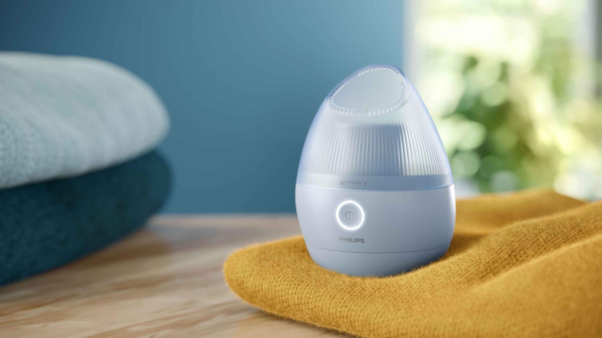 Philips Essentials apģērbu kopšanas līdzekļa tvaicētājs uz dzeltena džempera. Mazs, zils un moderns, tas atvieglo ātru tvaicēšanu. Jūs gaida svaigs, bez grumbām apģērbs.