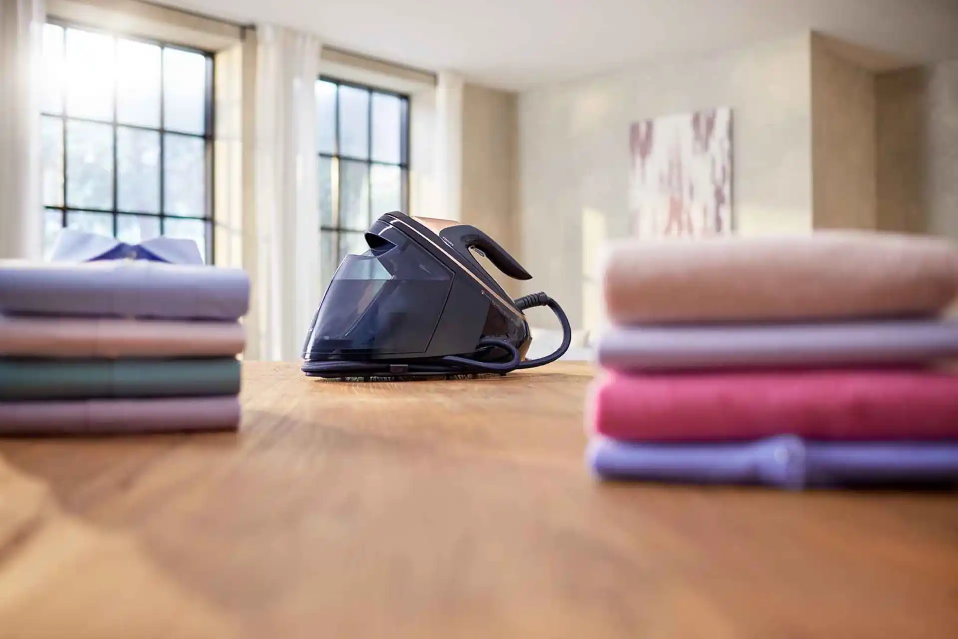 Studijas fotoattēls ar Philips tvaika gludināšanas sistēmu ar vara akcentiem un lielu ūdens tvertni. Apģērbi ir glīti sakrauti. Attēlā redzama profesionāla līmeņa apģērbu kopšana.