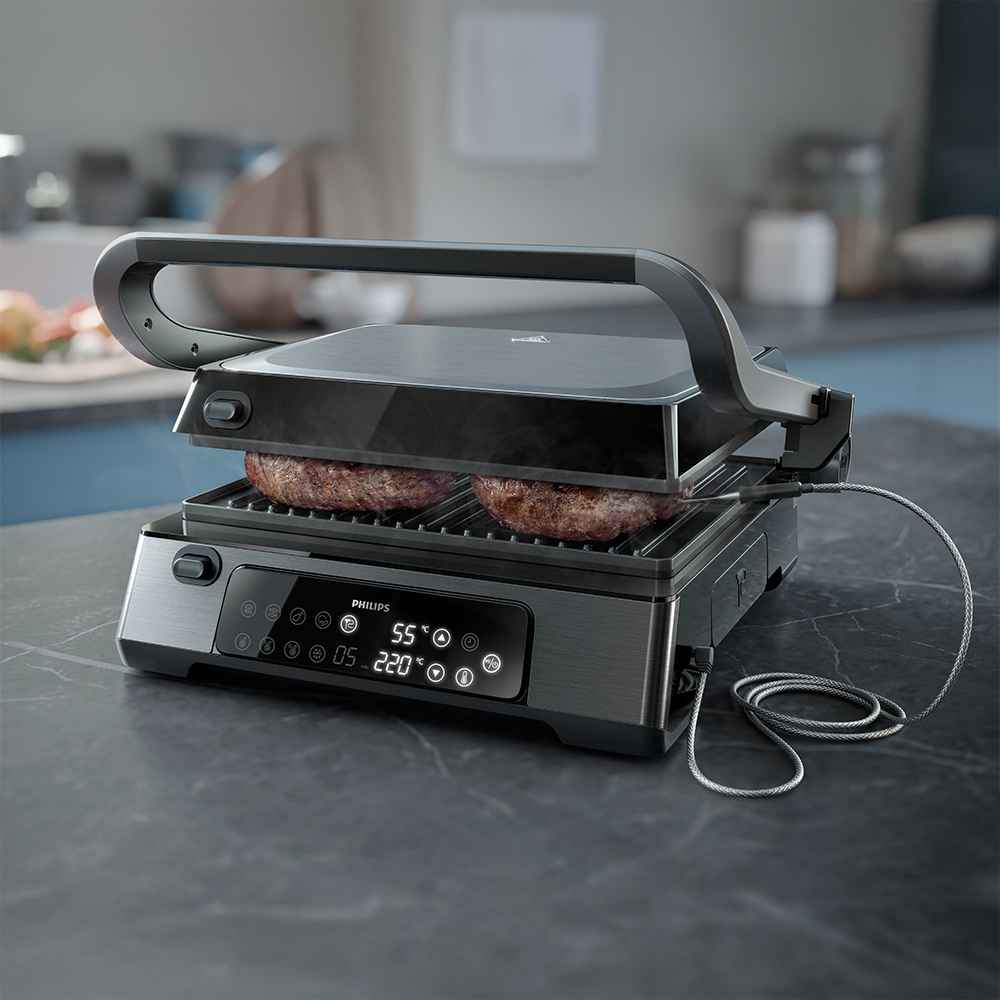 Philips grila un tosteru modeļa tuvplāns, kurā tie spiež burgeru kotletes. Digitālais displejs, temperatūras zonde un nepiedegošas plāksnes demonstrē šo augstākās kvalitātes grilu.