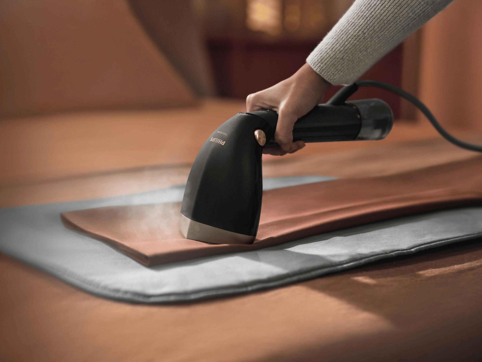 Gludināšana ar Philips 7000. sērijas rokas apģērba tvaicētāju uz auduma, izlīdzinot grumbas ar tvaiku. Ātra grumbu likvidēšana ar elegantu dizainu.