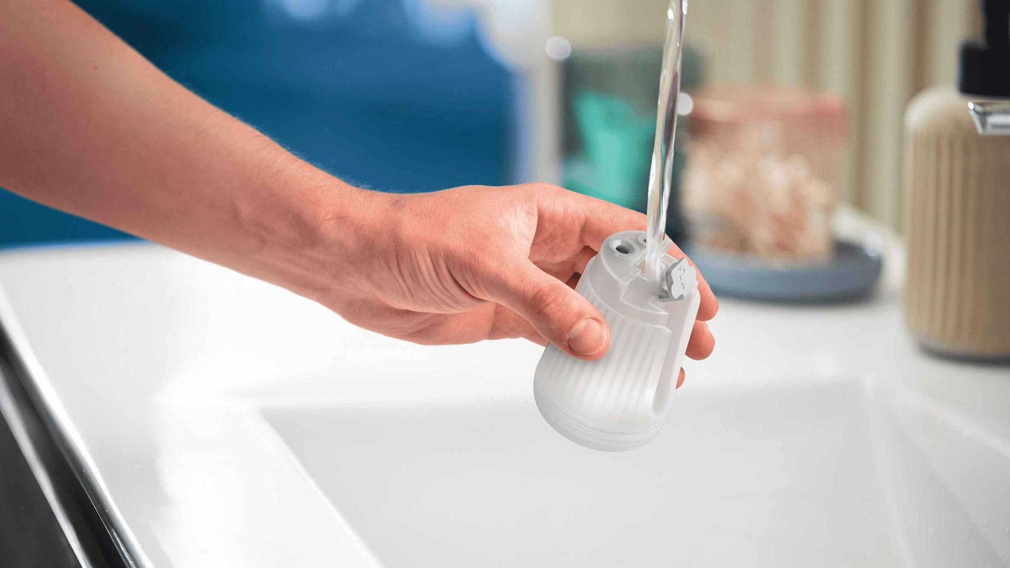 Philips rokas apģērba tvaicētāji: Caurspīdīga ūdens tvertne tiek uzpildīta ar rokām. Ilustrē Philips rokas tvaicētāja vienkāršo uzpildīšanas procesu, uzlabojot tā lietošanas ērtumu.