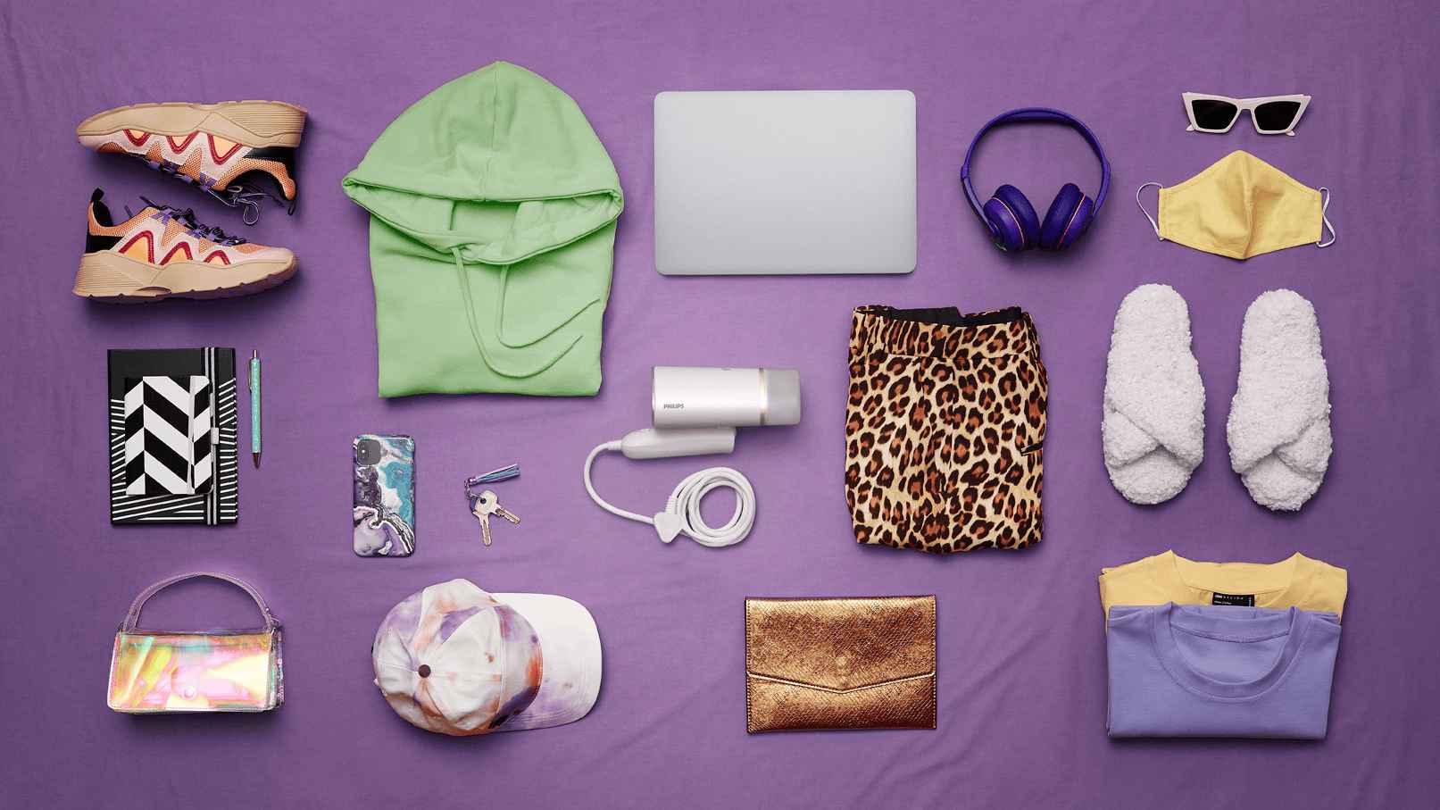 Modes aksesuāru, klēpjdatora un Philips rokas tvaika tvaika apģērba tvaicētājs plakans izkārtojums uz ceriņkrāsas. Kompozīcija ietver apavus, apģērbu, austiņas un personīgās higiēnas preces apģērba kopšanai.