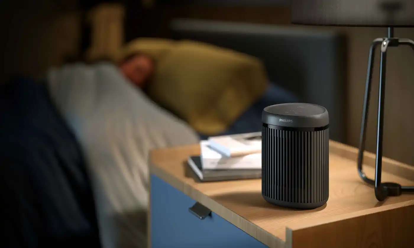 Philips sildītājs: elegants, melns gaisa attīrītājs uz naktsgaldiņa guļamistabā. Nodrošina izcilu klimata kontroli, garantējot ērtu un veselīgu miega vidi.