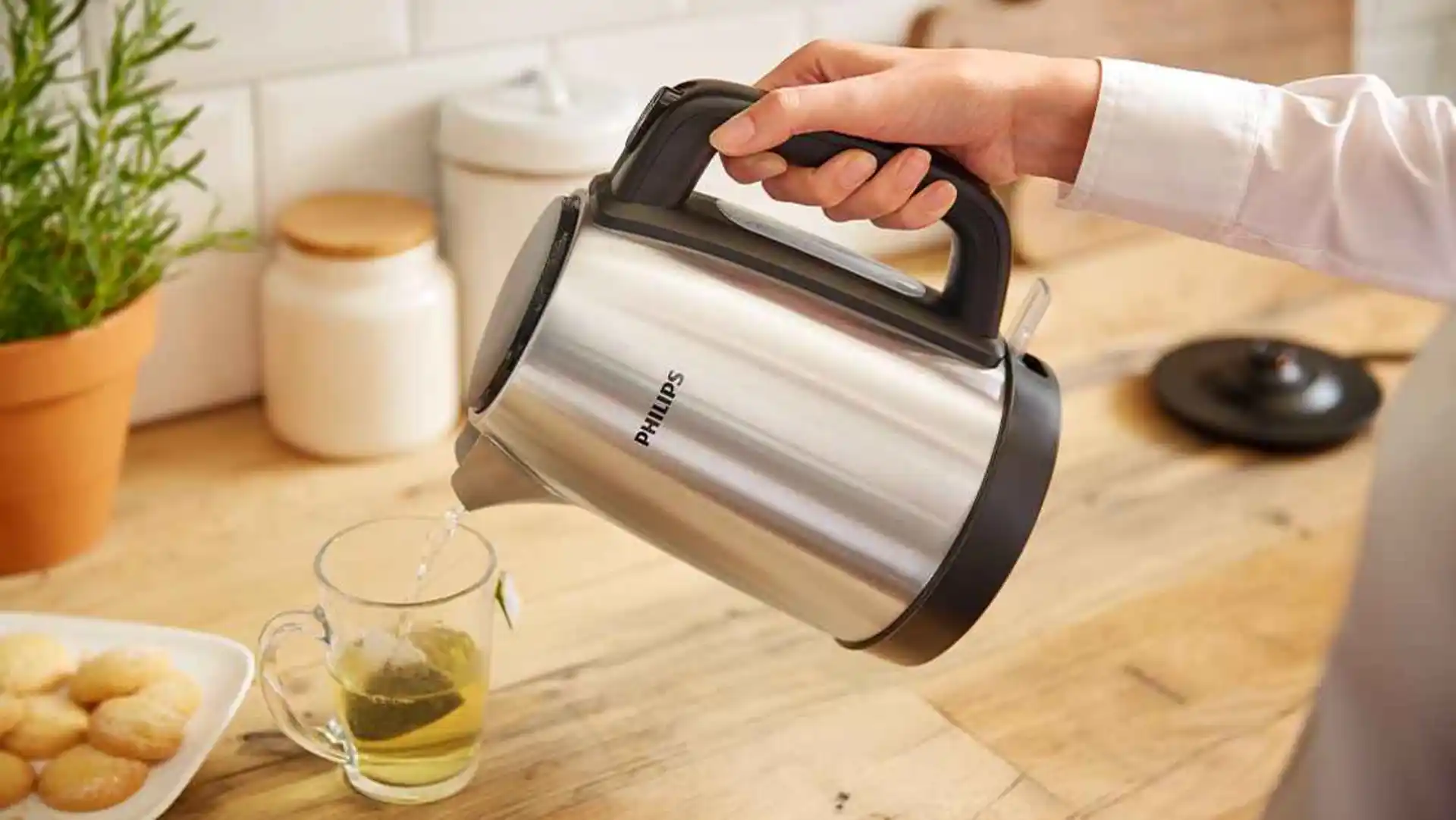 Ar rokām lejot ūdeni no eleganta Philips tējkannas modeļa ar matētu tēraudu, tiek nodrošināta nepārspējama lietotāja pieredze. Karsts ūdens plūst ar tēju piepildītā krūzē, kas novietota gaišā virtuvē.