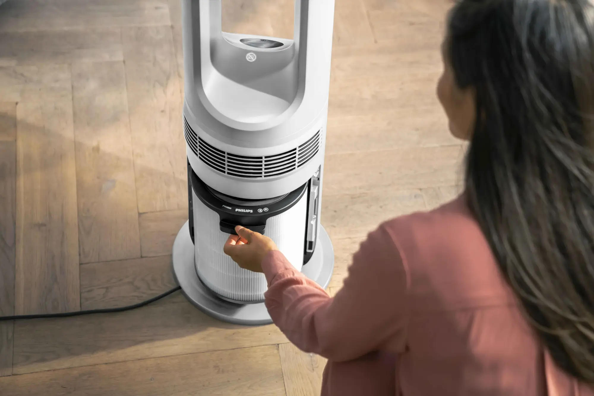 Cilvēks piekļūst filtram uz eleganta, balta Philips daudzfunkcionālā Climate Care torņa ventilatora optimālai mājas klimata pārvaldībai.