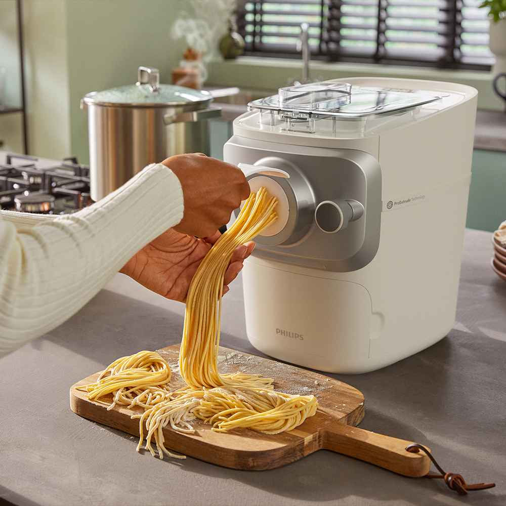 Philips pastas gatavotājs izspiež svaigus makaronus uz koka dēlīša; perfekti spageti bez piepūles pagatavo jūsu virtuvē. Izbaudiet izcilus rezultātus ar vieglumu.