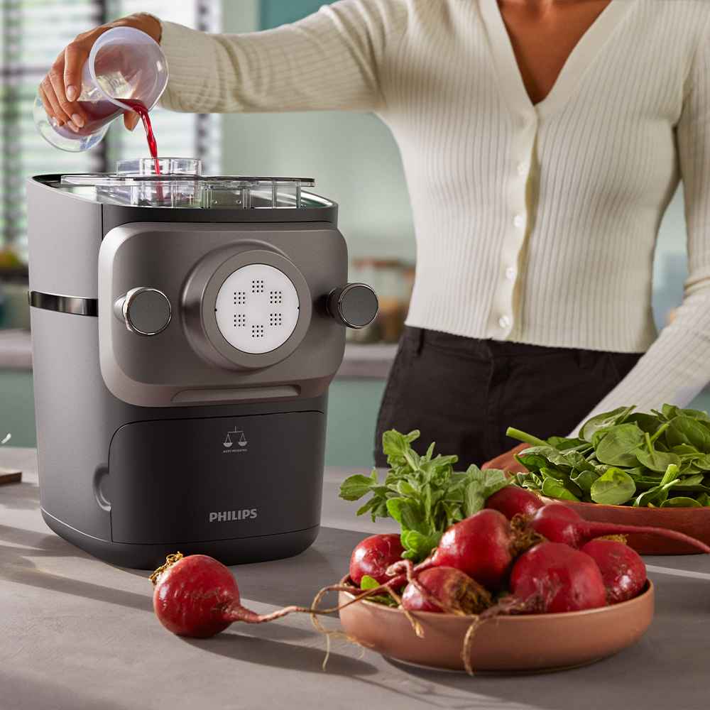 Sieviete ielej šķidrumu elegantā, pelēkā Philips virtuves pastas gatavotājā. Philips pastas gatavotāju līnija apvieno tehnoloģiju ar dizainu un izceļ svaigus, mājās gatavotus makaronus.