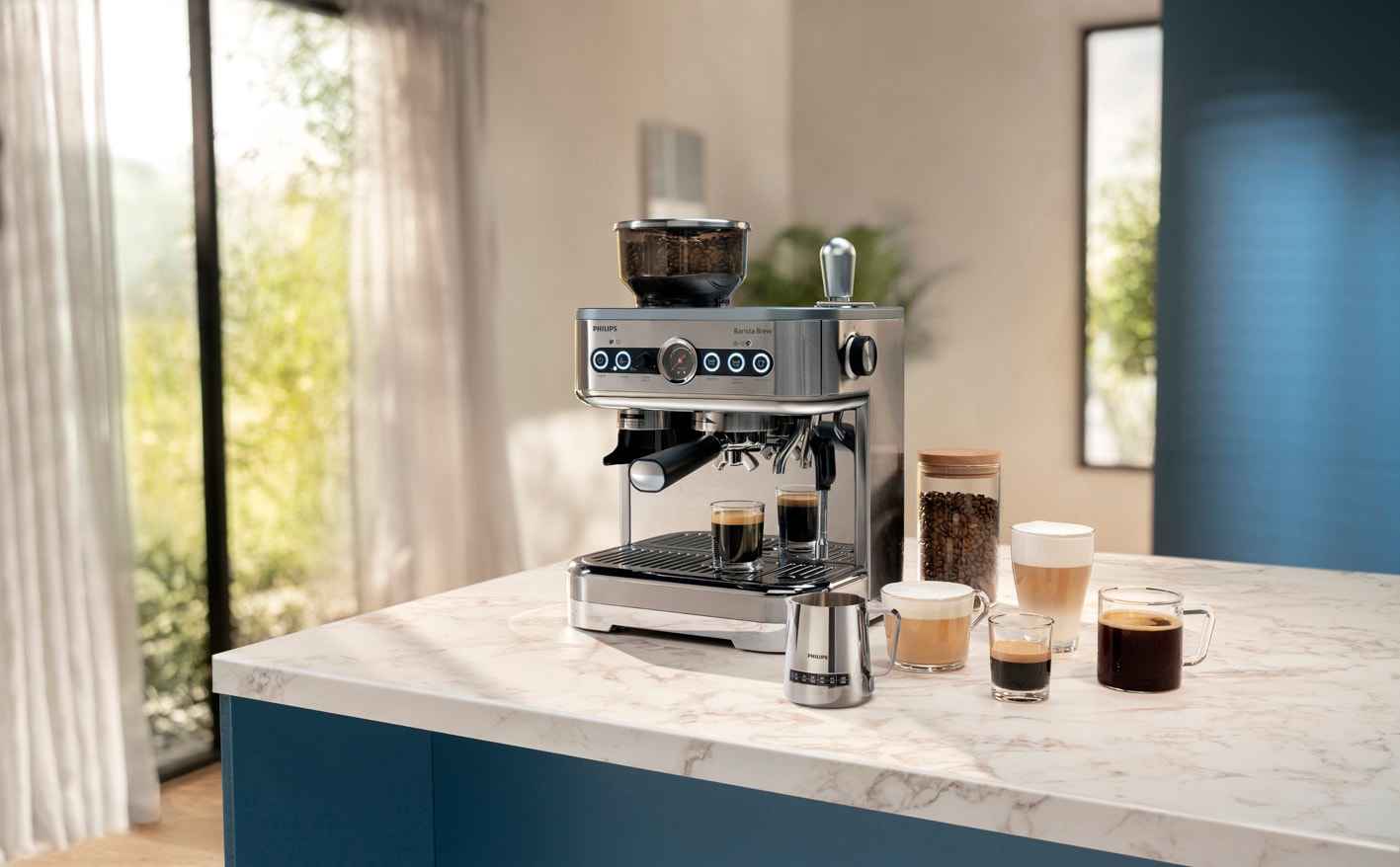 Philips pusautomātiskais kafijas automāts, mirdzoša nerūsējošā tērauda korpuss, uz marmora virsmas. Mākslinieciski sakārtoti kafijas dzērieni, dzirnaviņas un pupiņu krūka. Barista līmeņa pieredze.