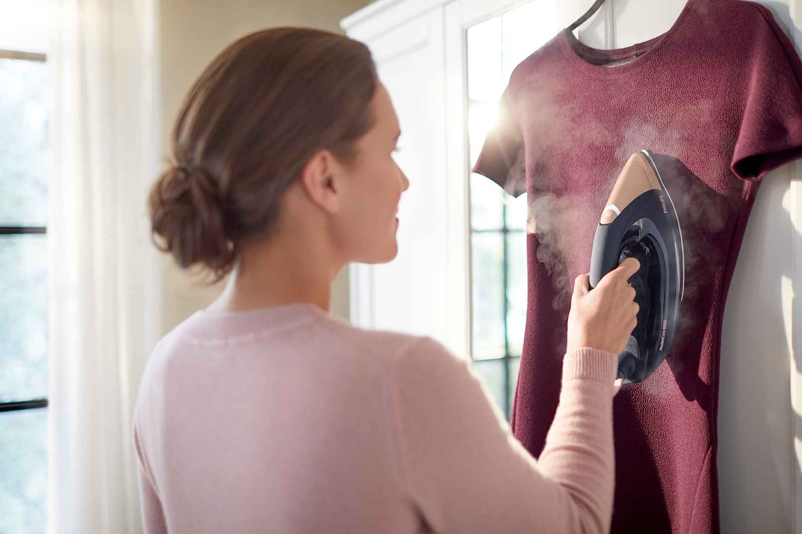 Sieviete izmanto Philips PerfectCare 9000 gludināšanas sistēmu, lai tvaicētu sarkanbrūnu kleitu. Izcils dizains nodrošina nepārspējamu lietotāja pieredzi. Gludināšana no jauna izgudrota.