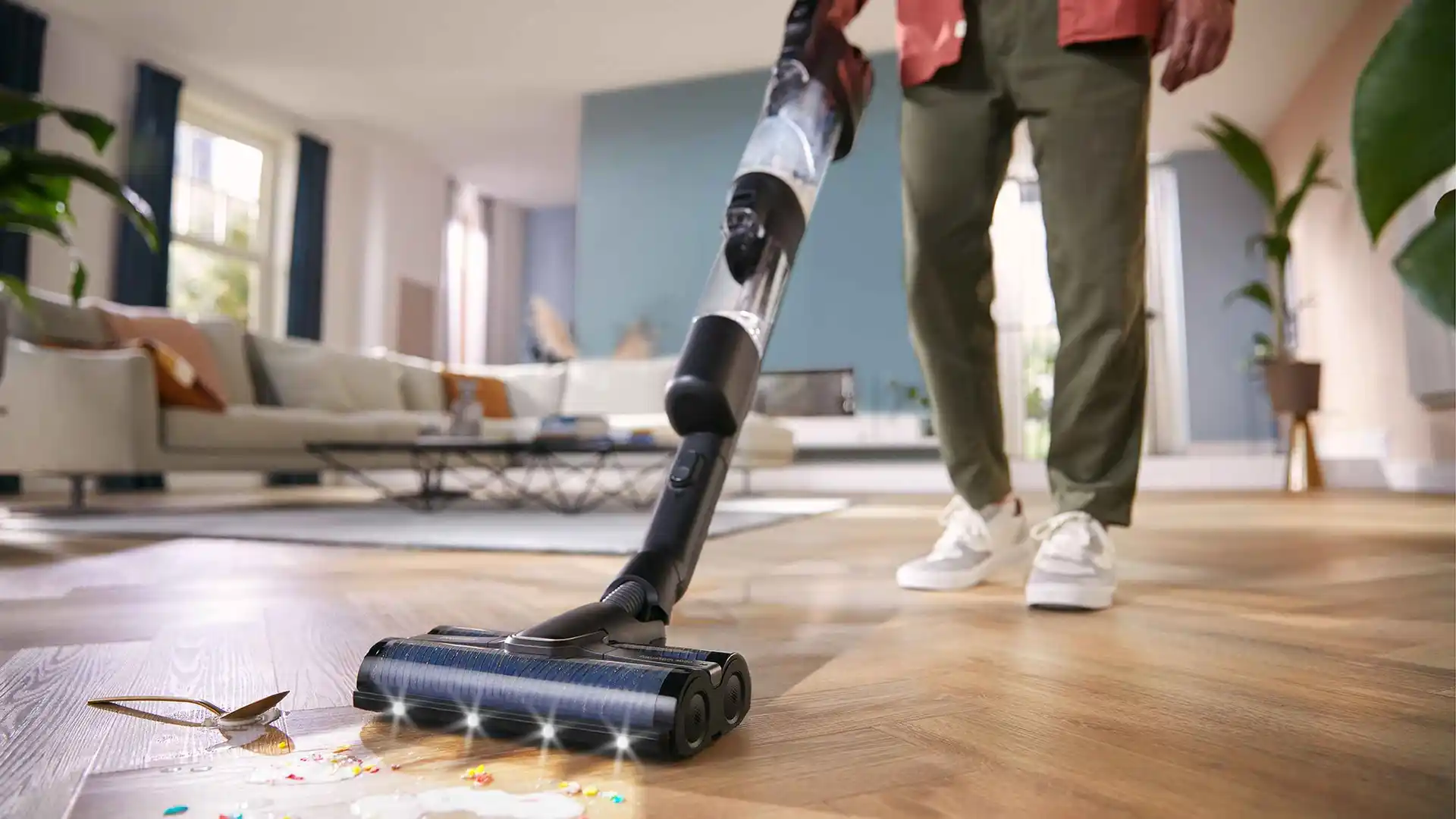 Cilvēks, kas izmanto Philips Vac & Wash bezvadu putekļsūcēju, bez piepūles notīra izlijušu ēdienu no koka grīdas. Ierīcei ir jaudīga sūkšanas jauda un spilgtas LED gaismas.
