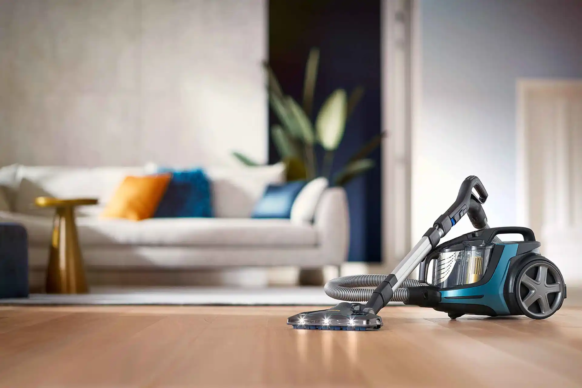 Philips putekļu sūcēji grīdas kopšanas līnija — jaunākās tehnoloģijas ar izcilu dizainu, LED apgaismojumu, caurspīdīgu putekļu tvertni un zilganzaļu korpusu uz koka grīdas.