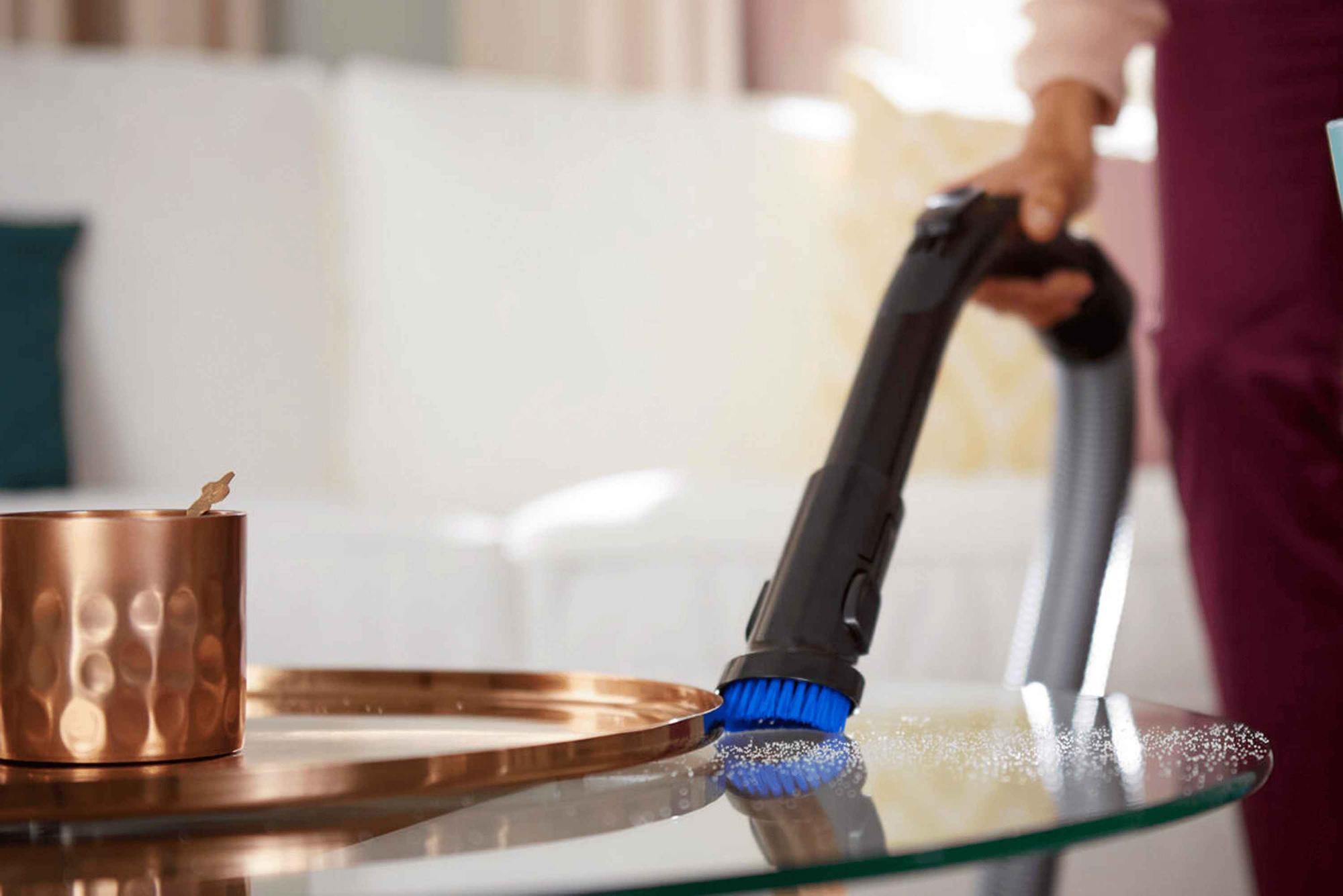 Philips putekļu sūcēji: meistarīgi noņem putekļus no stikla galda, izmantojot zilu birsti, demonstrējot izcilu tīrību un dizainu.