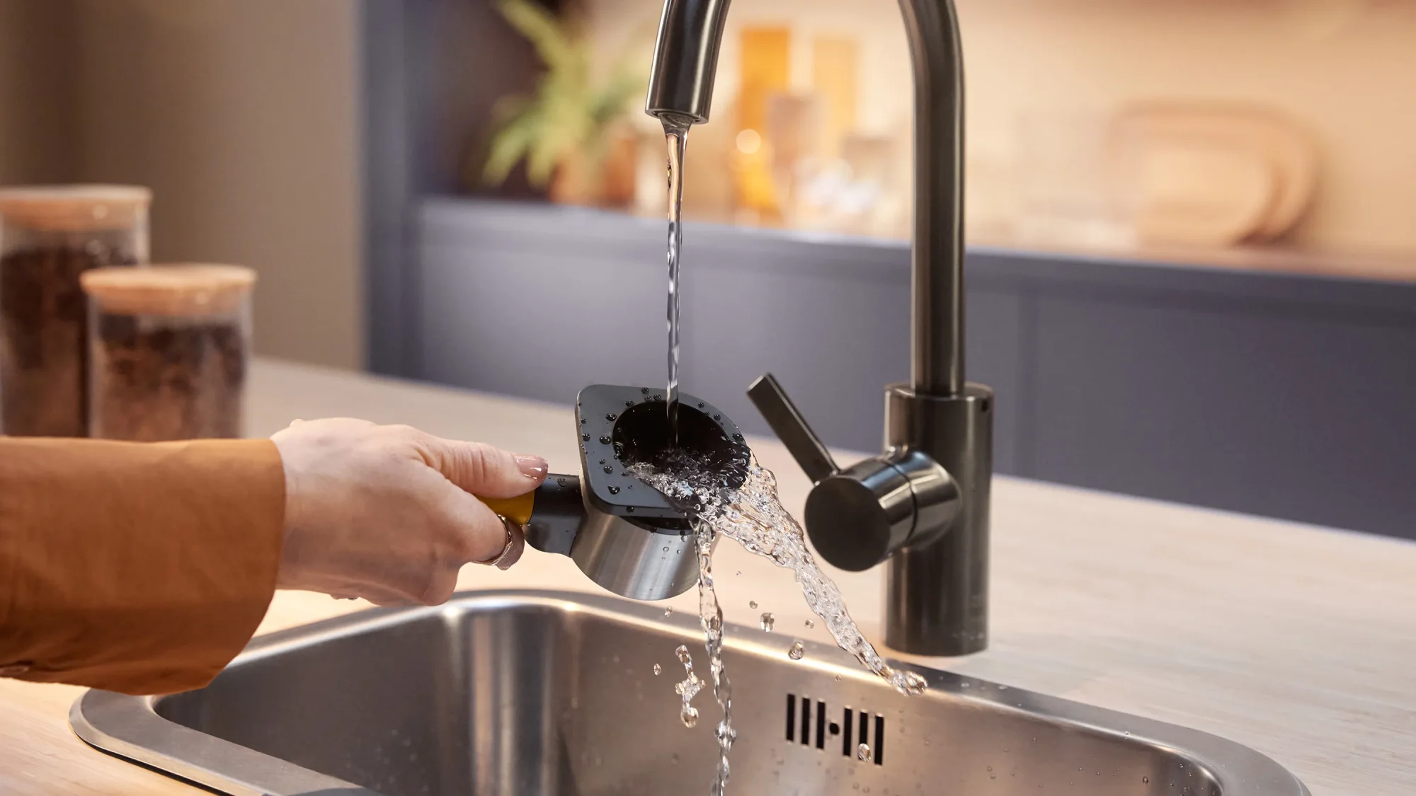 Persona zem krāna skalo kafijas biezumus no Philips Baristina kafijas automāta portafiltra. Vienkārša augstākās kvalitātes kafijas automāta tīrīšana modernas virtuves izlietnē.